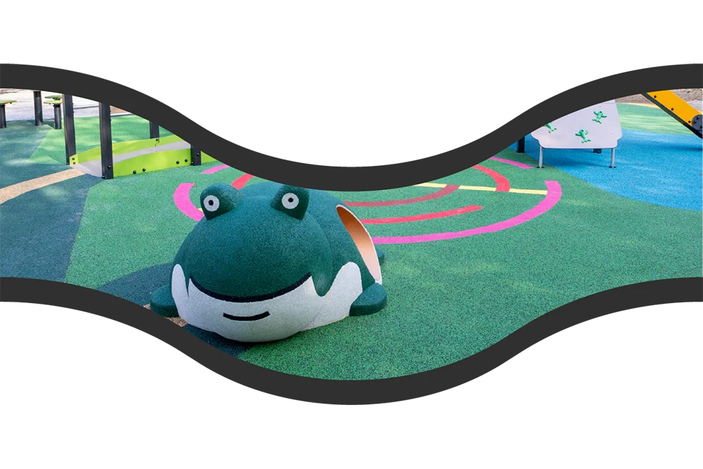 A playground with a green frog-shaped play structure sits on vibrant rubber surfacing, showcasing creative rubber surfacing applications for playgrounds and commercial spaces, with curved lines and play equipment in the background.