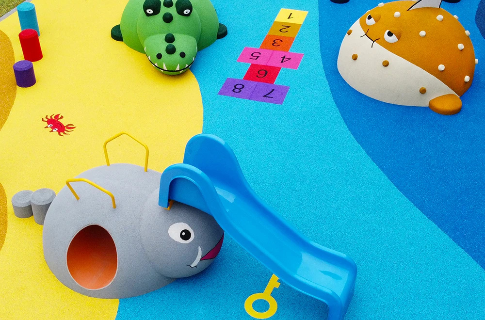 Colorful playground featuring animal-themed structures—a fun elephant slide, crocodile, and fish—set on blue and yellow rubber surfacing applications for playgrounds, complete with a vibrant hopscotch grid.