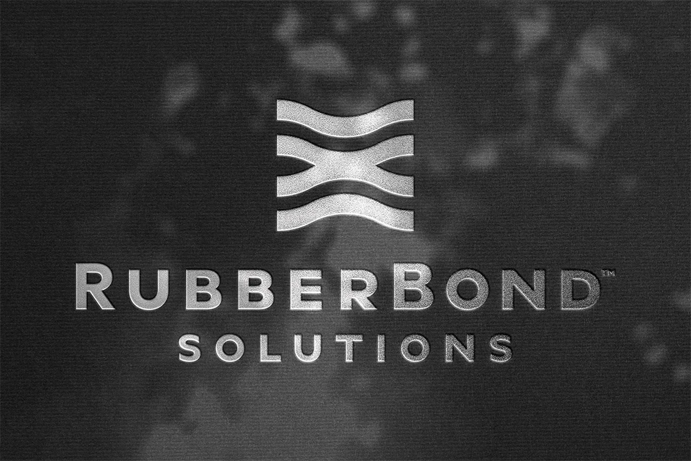 RubberBond Solutions logo with a metallic finish, featuring three wavy lines above the company name on a textured dark background—ideal for rubber surfacing applications for playgrounds and commercial spaces.