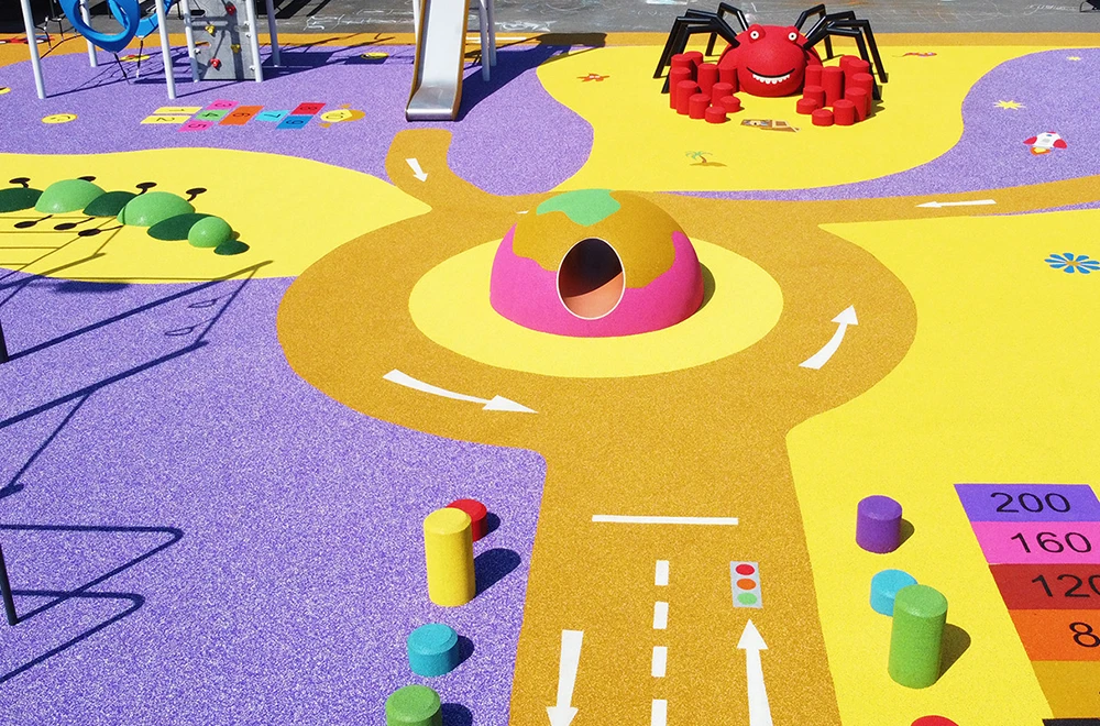 Colorful playground with a yellow and purple rubber surface, featuring a tunnel, a red spider structure, caterpillar shapes, educational markings, and showcasing innovative rubber surfacing applications for playgrounds and commercial spaces.