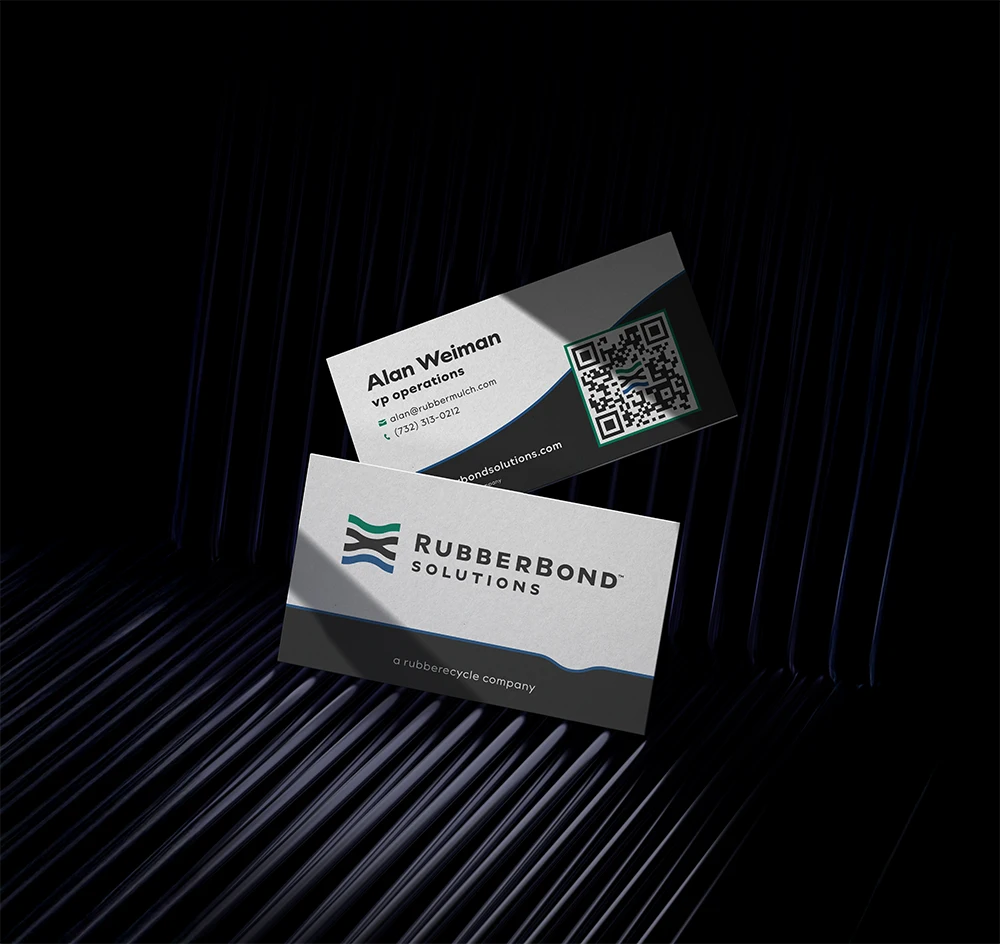 Two business cards for RubberBond Solutions, specializing in rubber surfacing applications for playgrounds and commercial spaces, featuring a logo, company name, and contact info for Alan Weiman, VP of operations, displayed on a dark, ridged surface.