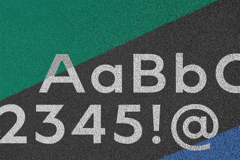 White letters, numbers, and symbols are displayed on a textured surface enhanced for rubber surfacing applications for playgrounds and commercial spaces, with green, black, and blue diagonal color blocks in the background.
